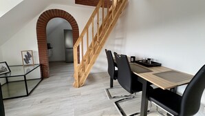 Un comedor con una escalera de madera, un arco de ladrillo y una cocina moderna al fondo.