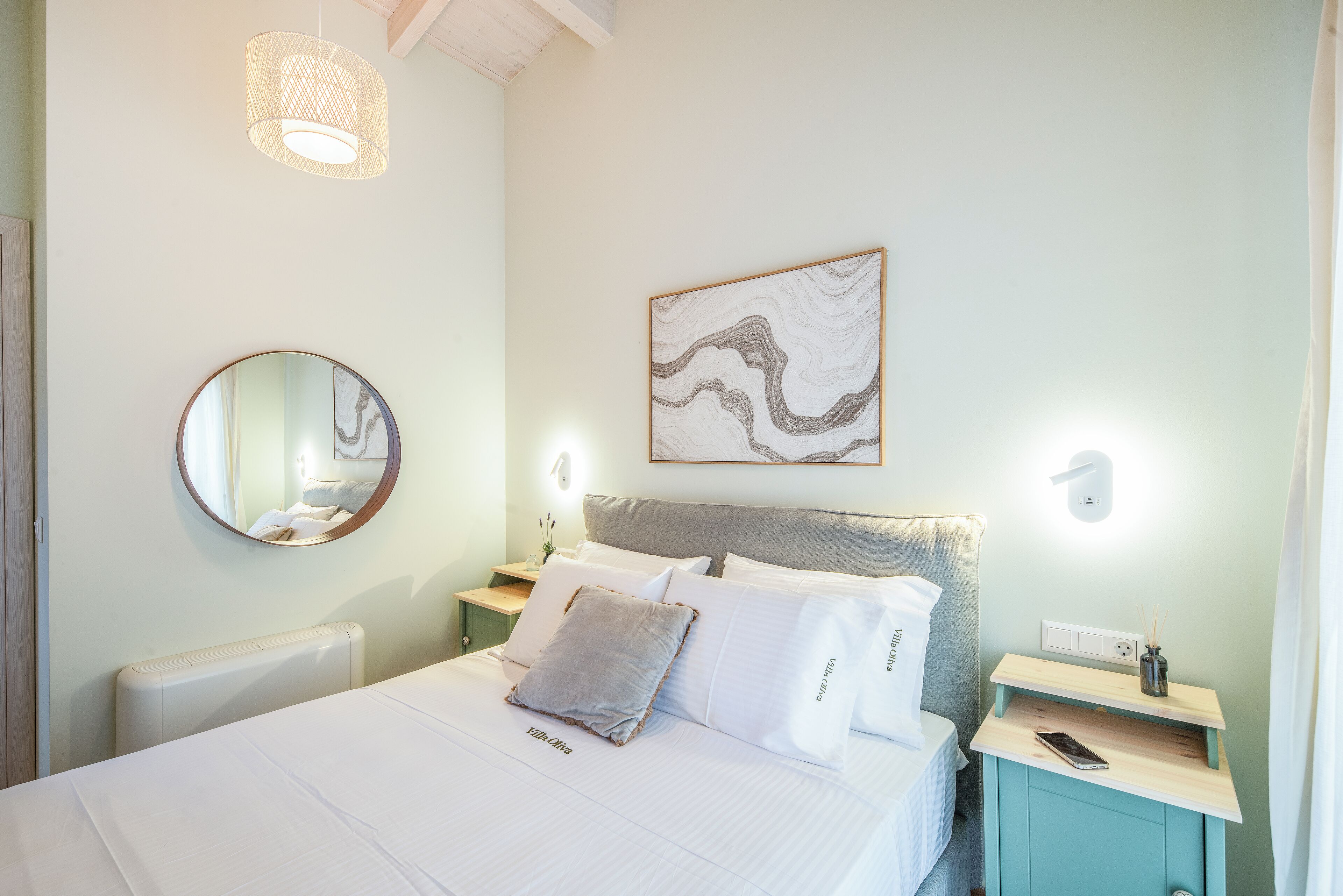 A neatly arranged bedroom with a bed, bedside tables, a mirror, and a wall-mounted light fixture.