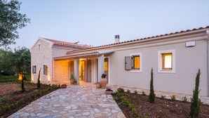 Ein gepflasterter Weg führt zu einem Haus mit Ziegeldach, einer Veranda und Topfpflanzen.