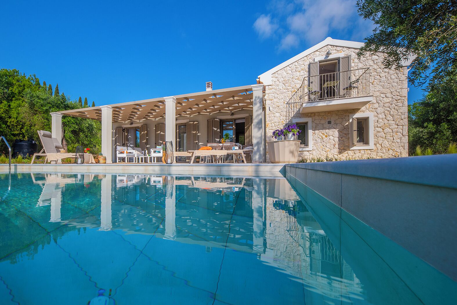 A poolside area with lounge chairs, a covered seating area, and a stone building with a balcony.
