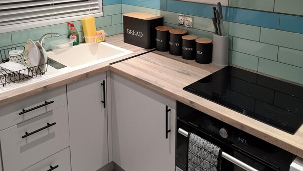 A modern kitchen with a black stove, white cabinets, and a tiled backsplash. - Agape Hubs (Barnstone)