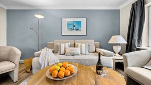 A modern living room with a round wooden coffee table, a sofa set, a floor lamp, and a framed picture on the wall. - Tinkas Kate - Charming bungalow with garden in Westerland, Sylt (Sylt)