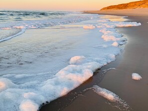 Ein Strand mit Wellen, die das Ufer erreichen, einem klaren Himmel und einer entfernten Klippe.