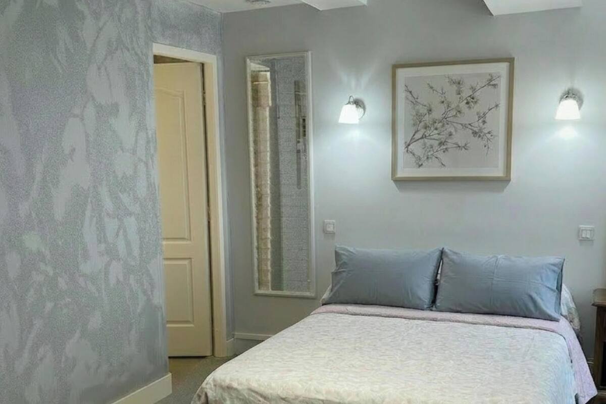 Une chambre à coucher avec un lit, une porte, une lampe fixée au mur et un tableau encadré.