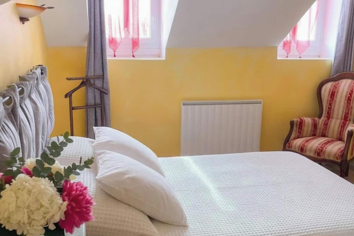 Une chambre à coucher avec un lit, une chaise, un radiateur et une fenêtre avec des rideaux.