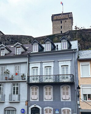 A multi-story building with a stone tower, balconies with metal railings, and a sign indicating a parking area. - La Rose du Château (Lourdes)