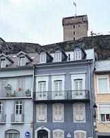Un edificio de varios pisos con una torre de piedra, balcones con barandillas de metal y un letrero que indica un estacionamiento.