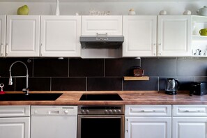 Une cuisine avec des armoires blanches, une hotte de cuisinière en acier inoxydable, un plan de travail en bois, un lave-vaisselle et une machine à café.