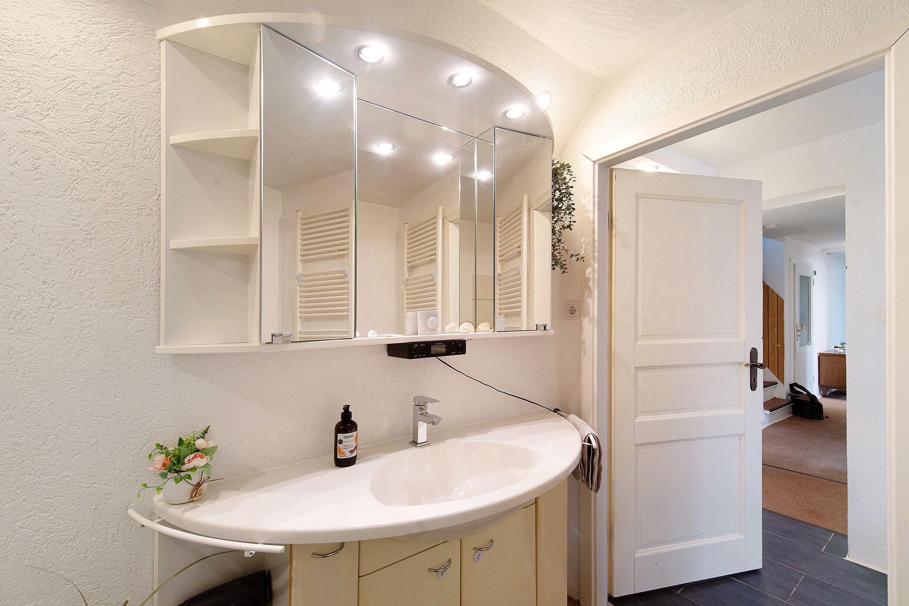 A bathroom with a white sink, a mirror, and a door leading to another room.