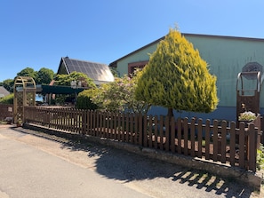Un bâtiment à l’extérieur verdoyant, avec une clôture en bois et un arbre devant.