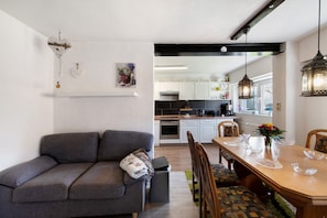 A modern living room with a grey sofa, a dining table set for four, and a kitchen in the background.