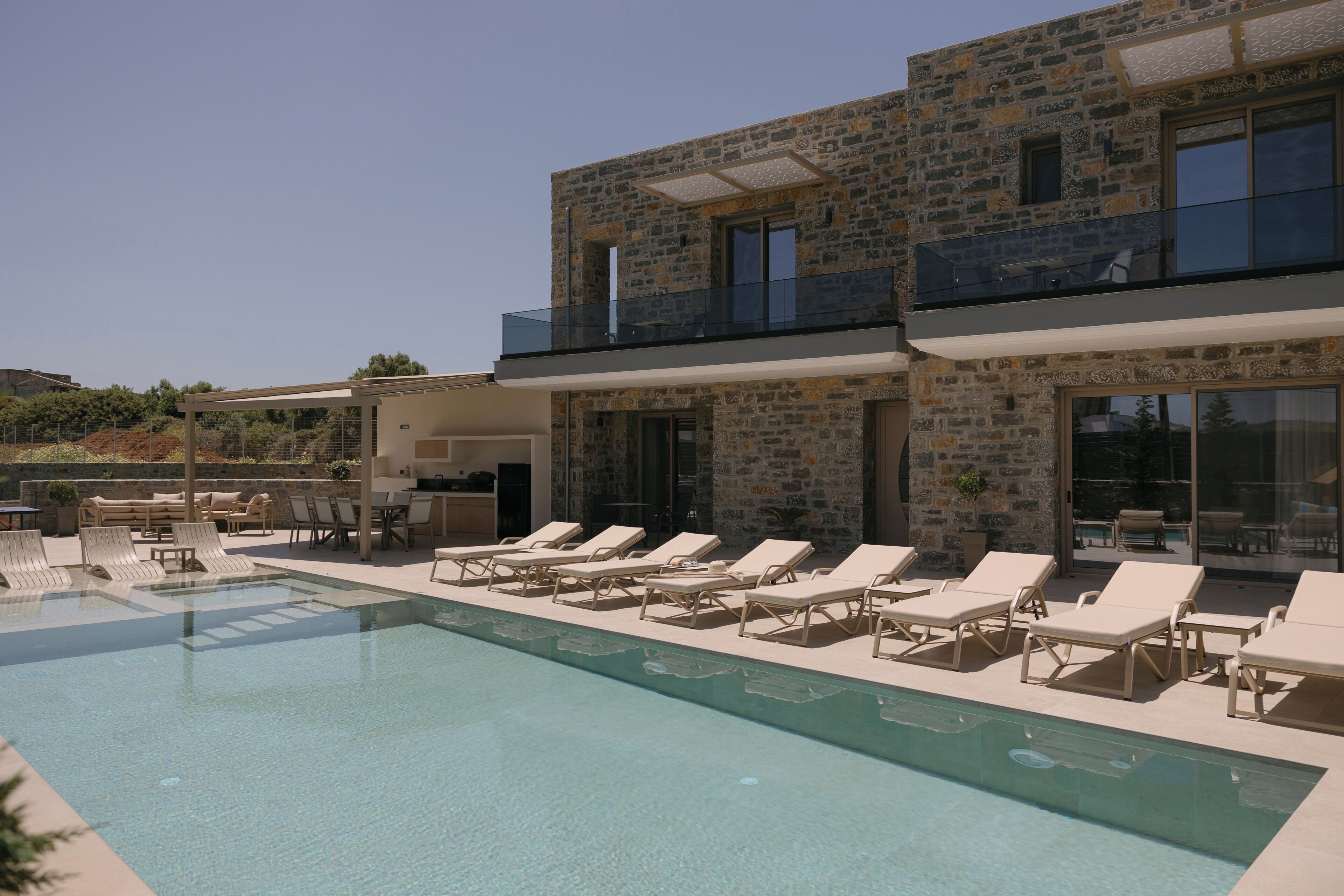 A modern two-story building with a swimming pool, sun loungers, and a covered outdoor seating area.