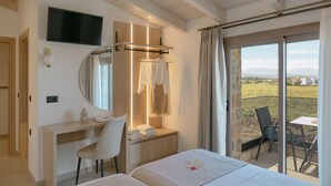Habitación de hotel con cama, escritorio, silla, televisor, espejo, zona de ducha y balcón con mesa y sillas.