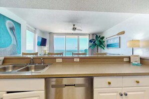 A modern kitchen with stainless steel appliances, a large window with a view, and a ceiling fan. - Gulfside Getaway 915–Beachfront–Sleeps 5 (Panama City Beach)