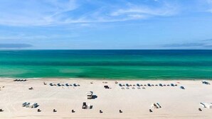 Una platja amb files de gandules i ombrel·les, un cel blau clar i aigües turqueses tranquil·les.