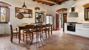 A rustic kitchen with a wooden table and chairs, a hanging light fixture, and a stove. - Il Focolare – Spacious Apartment in Farmhouse with Private Terrace and Pool (Pelago)