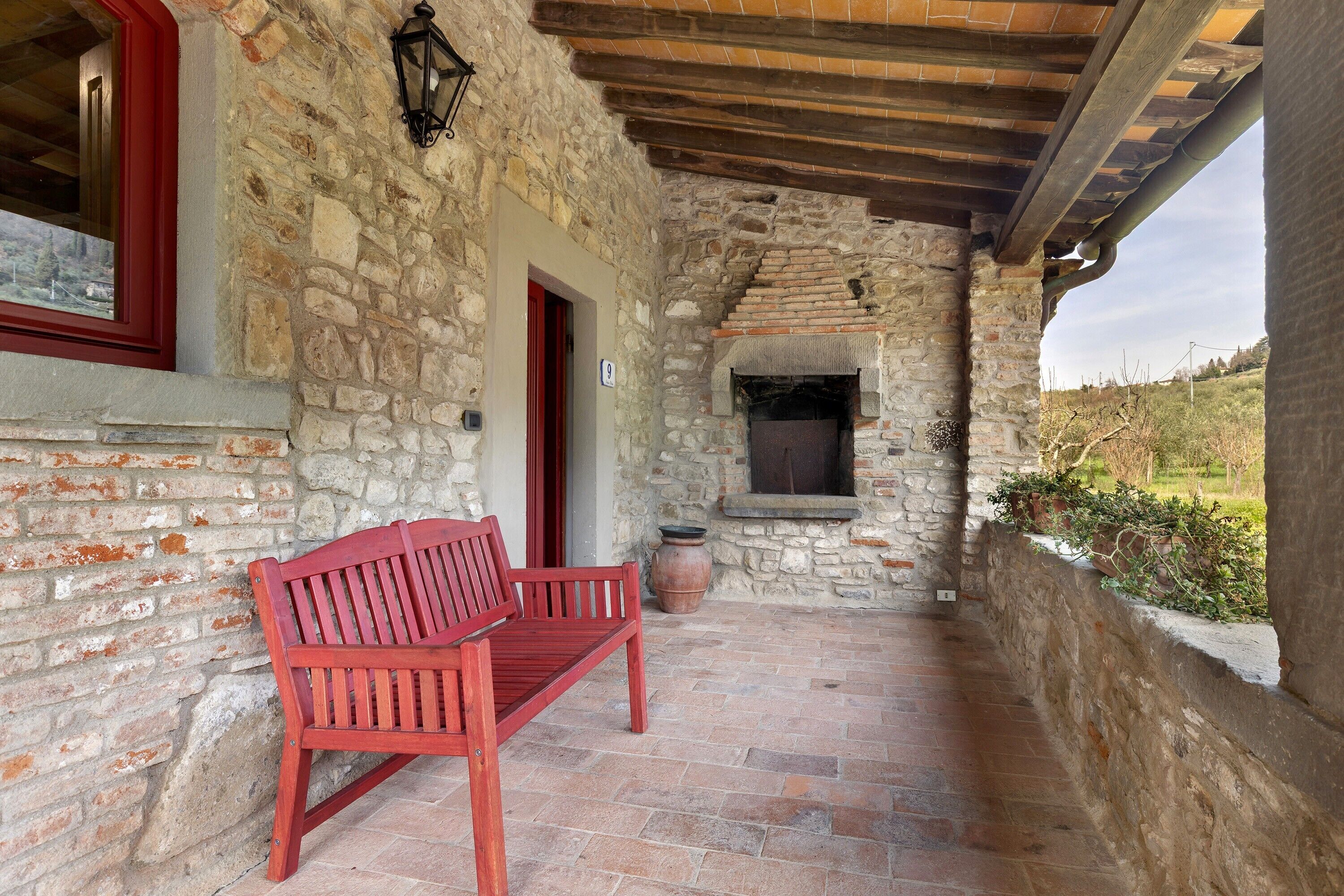 A stone-walled outdoor area with a red bench, a small fireplace, and a window with a red frame.