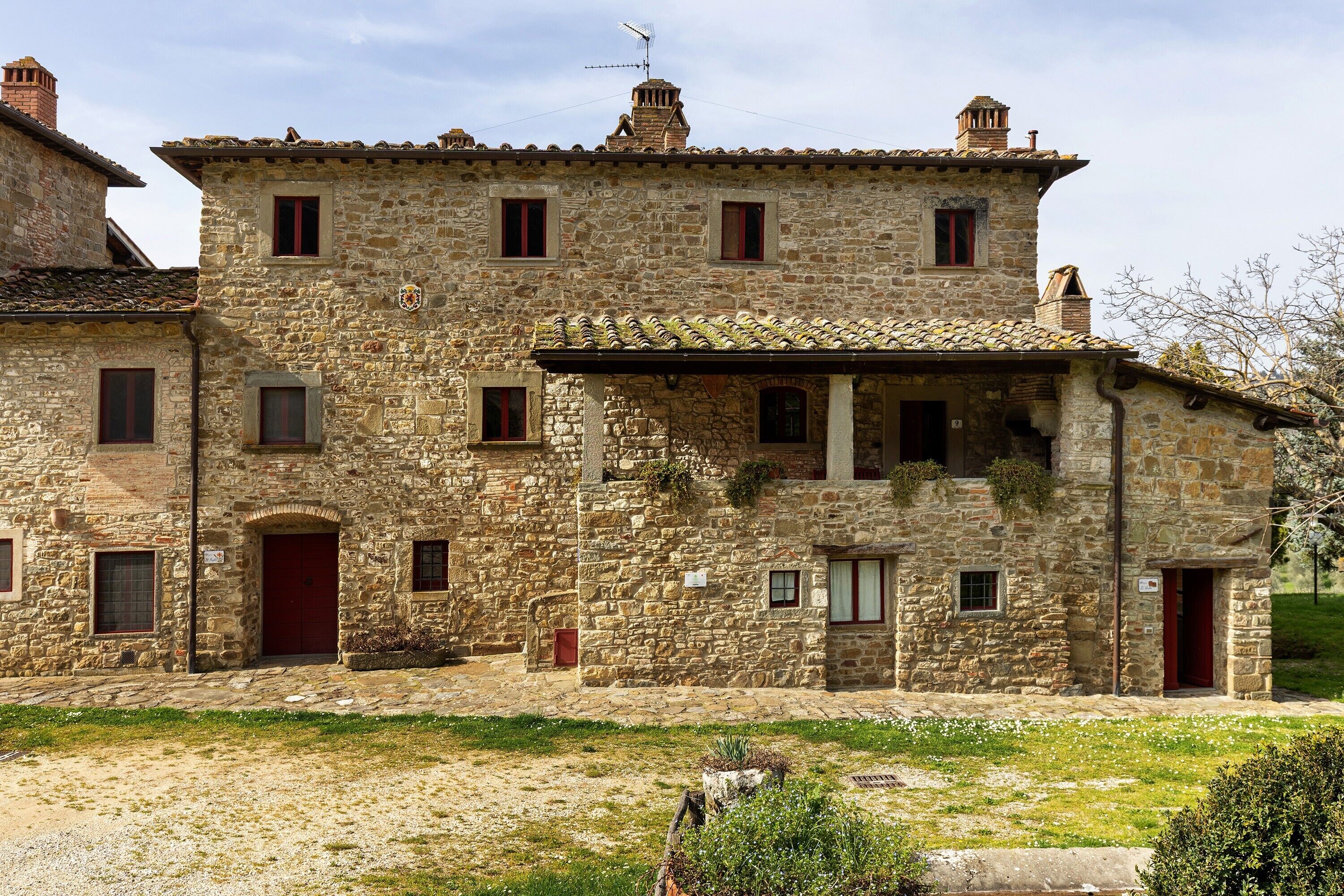 Un edificio de piedra con múltiples ventanas y puertas, techo de tejas y un pequeño jardín delantero.