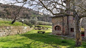 A stone building with a rustic appearance, a grassy area with a bench, and a tree in the foreground. - Il Focolare – Spacious Apartment in Farmhouse with Private Terrace and Pool (Pelago)