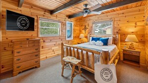 A wooden cabin bedroom with a bed, dresser, vanity, and a ceiling fan. - Bass Bay Getaway | Lakefront Family Cottage (Elk Rapids)