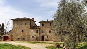 A stone building with multiple windows and a red door, surrounded by greenery and a gravel path. - La Torre – Panoramic Apartment in Farmhouse with Pool (Pelago)