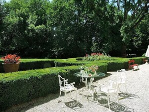 A garden with neatly trimmed hedges, a table with chairs, and potted plants.