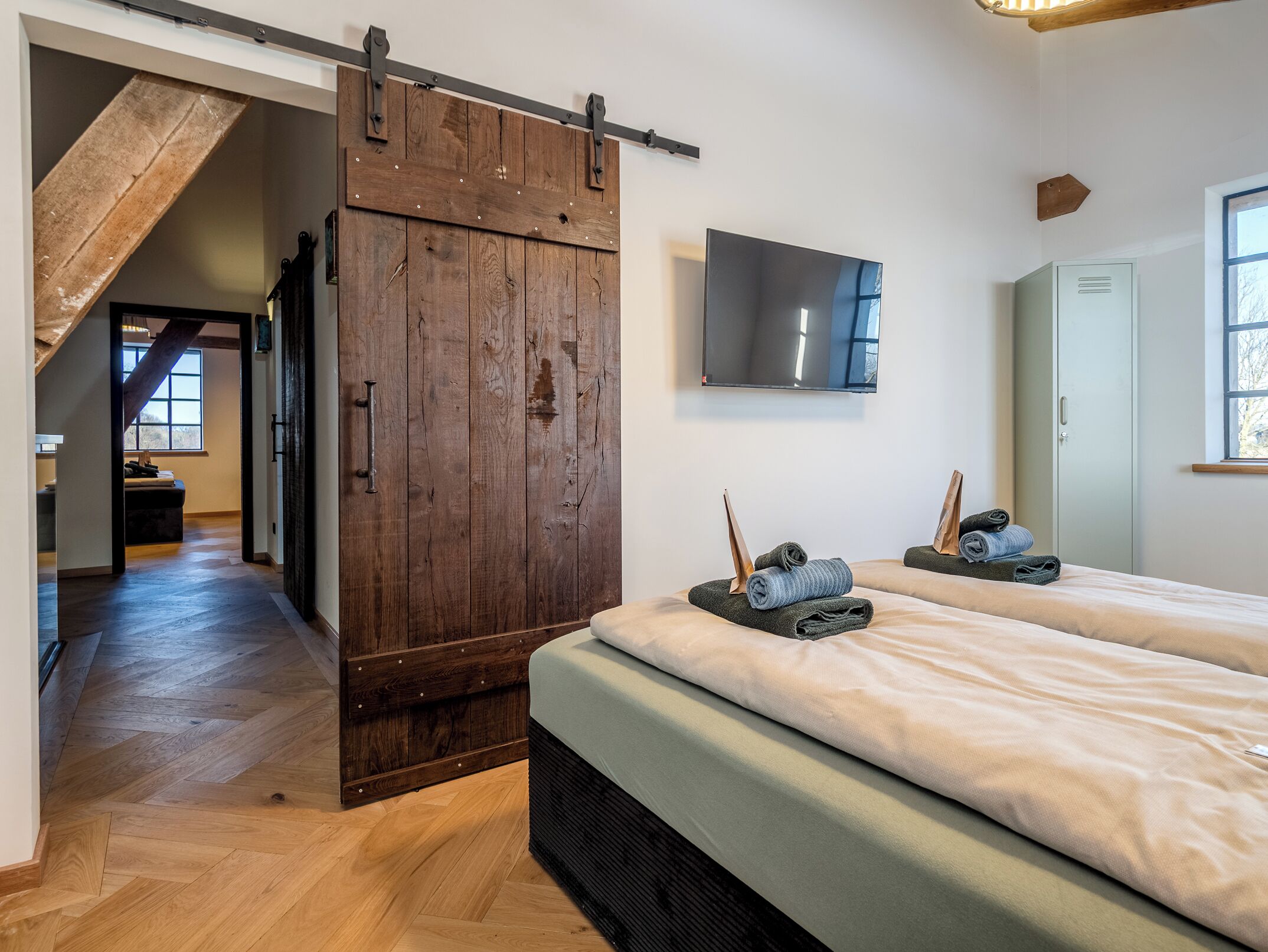 A bedroom with a sliding barn door, a bed with neatly folded towels, a mounted TV, and a wardrobe.