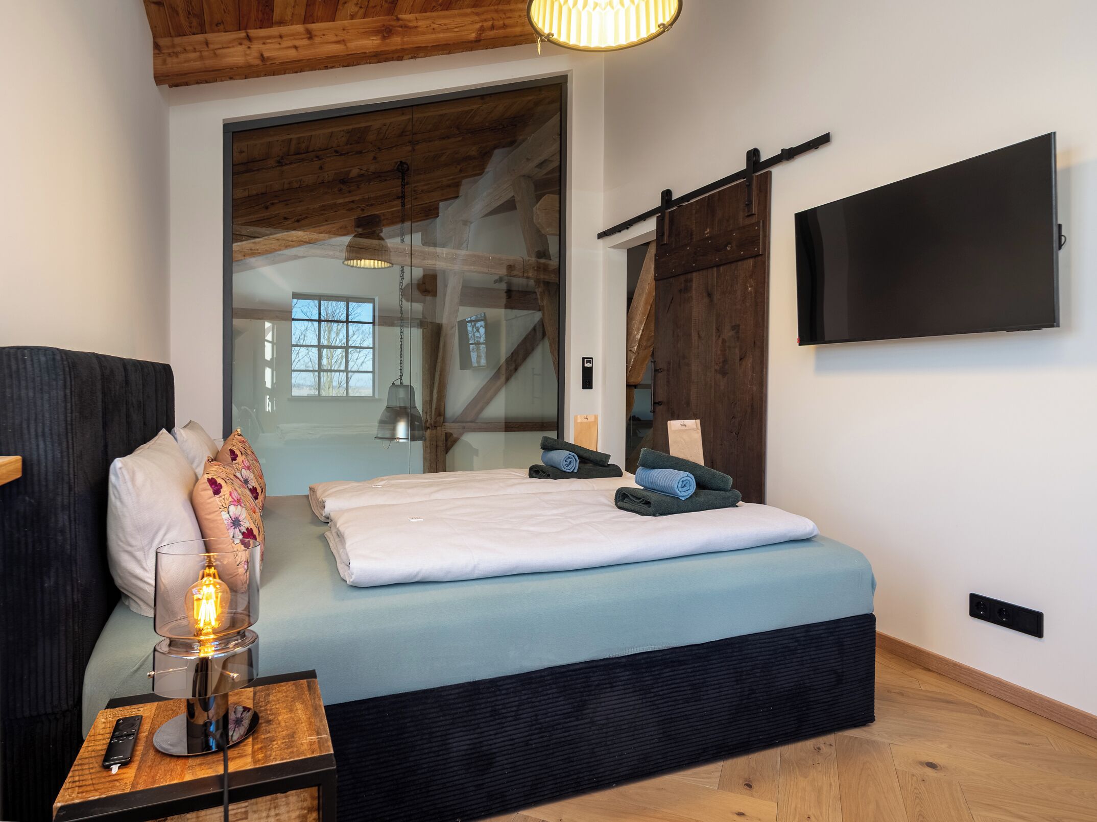 Un dormitorio con cama, televisor, lámpara y techo de madera.