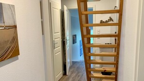Käytävällä on puinen tikapuu, joka johtaa ylätasanteelle, valkoinen ovi ja pieni jakkara.
