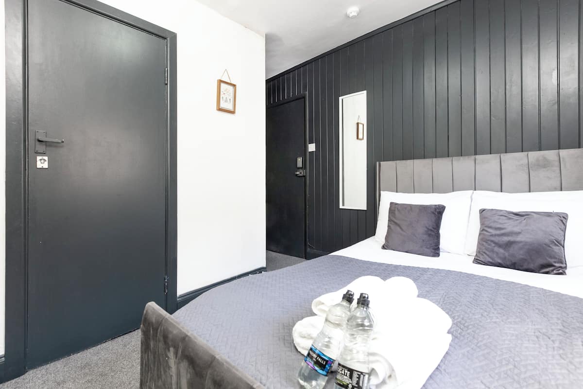 Ein Hotelzimmer mit einem Bett, einer dunklen Tür, einer weißen Wand und einem gerahmten Bild.