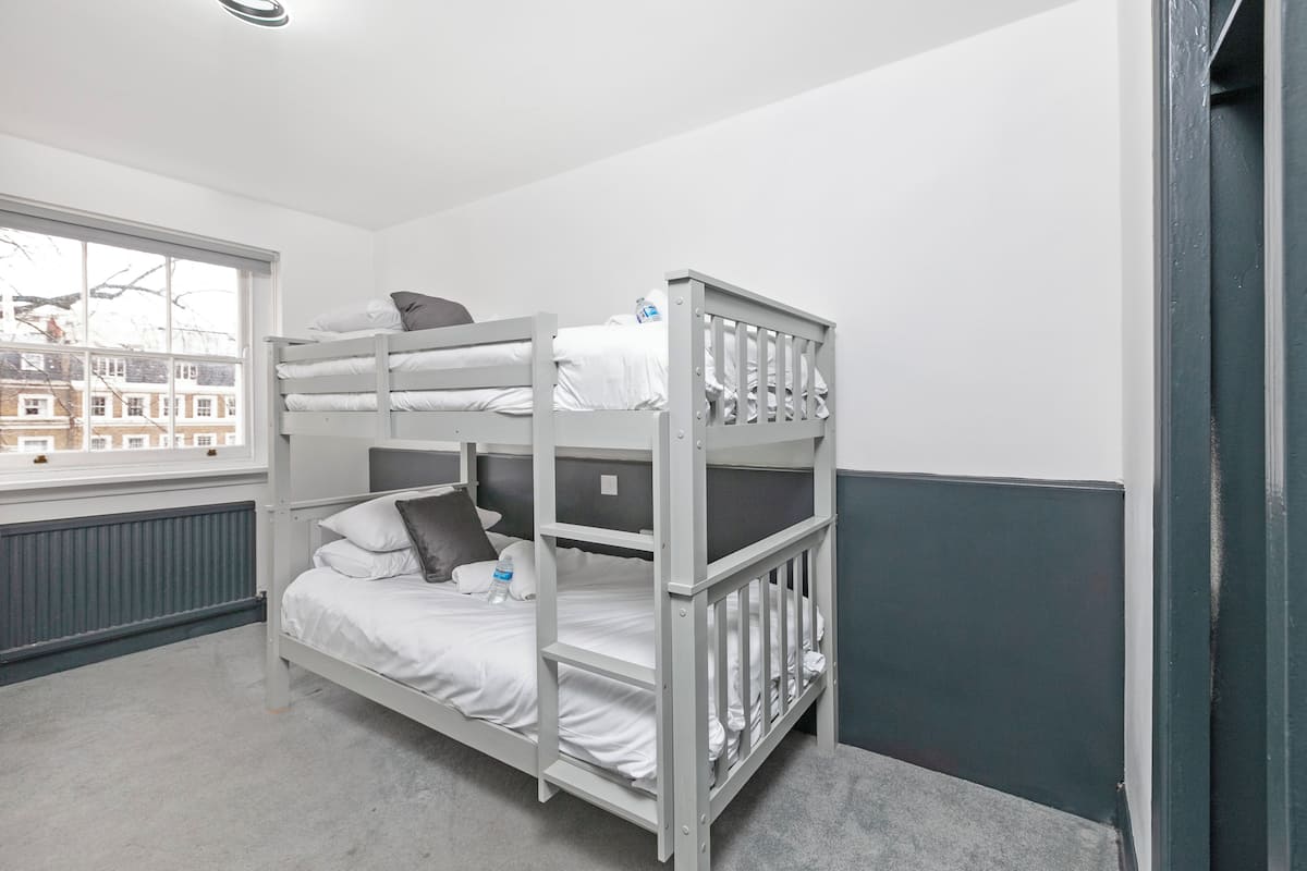 Ein Schlafraum mit Etagenbett, Fenster, Heizkörper und Tür.
