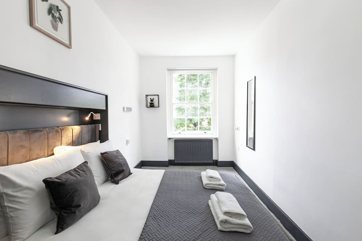 Ein Schlafzimmer mit Bett, Kissen, Kopfteil, Fenster und Heizkörper.