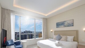 Ein Hotelzimmer mit einem großen Bett, einem Fernseher, einem Schreibtisch und Blick auf die Stadt.