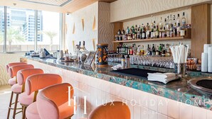Eine Bar mit Marmorplatte, mehreren Spirituosenflaschen, Gläsern und orangefarbenen Barhocker.