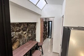 A narrow hallway with a stone wall, a wooden table with chairs, and a modern kitchen area with a stainless steel refrigerator. - Modern Cozy Apartment in the Heart of the City (San Salvador)