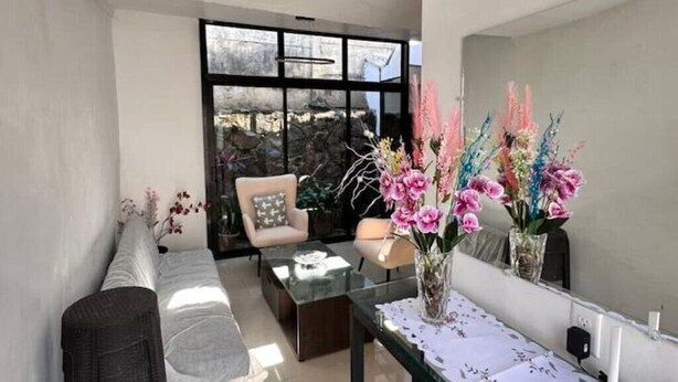 A modern living room with a sofa, two armchairs, a glass coffee table, and a vase with flowers.