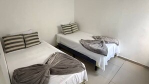 A room with three single beds, each with a white mattress and striped pillows.