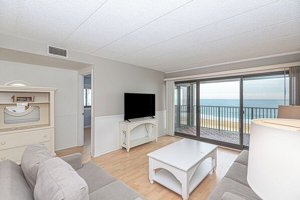 A living room with a television, a sofa, a coffee table, and a view of the beach. - Remodel 2BD/2 bath direct Ocean Front condo  with outdoor pool (Ocean City)