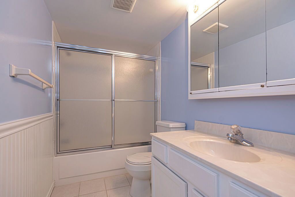 A bathroom with a glass-enclosed shower, a toilet, and a sink with a mirror above it.