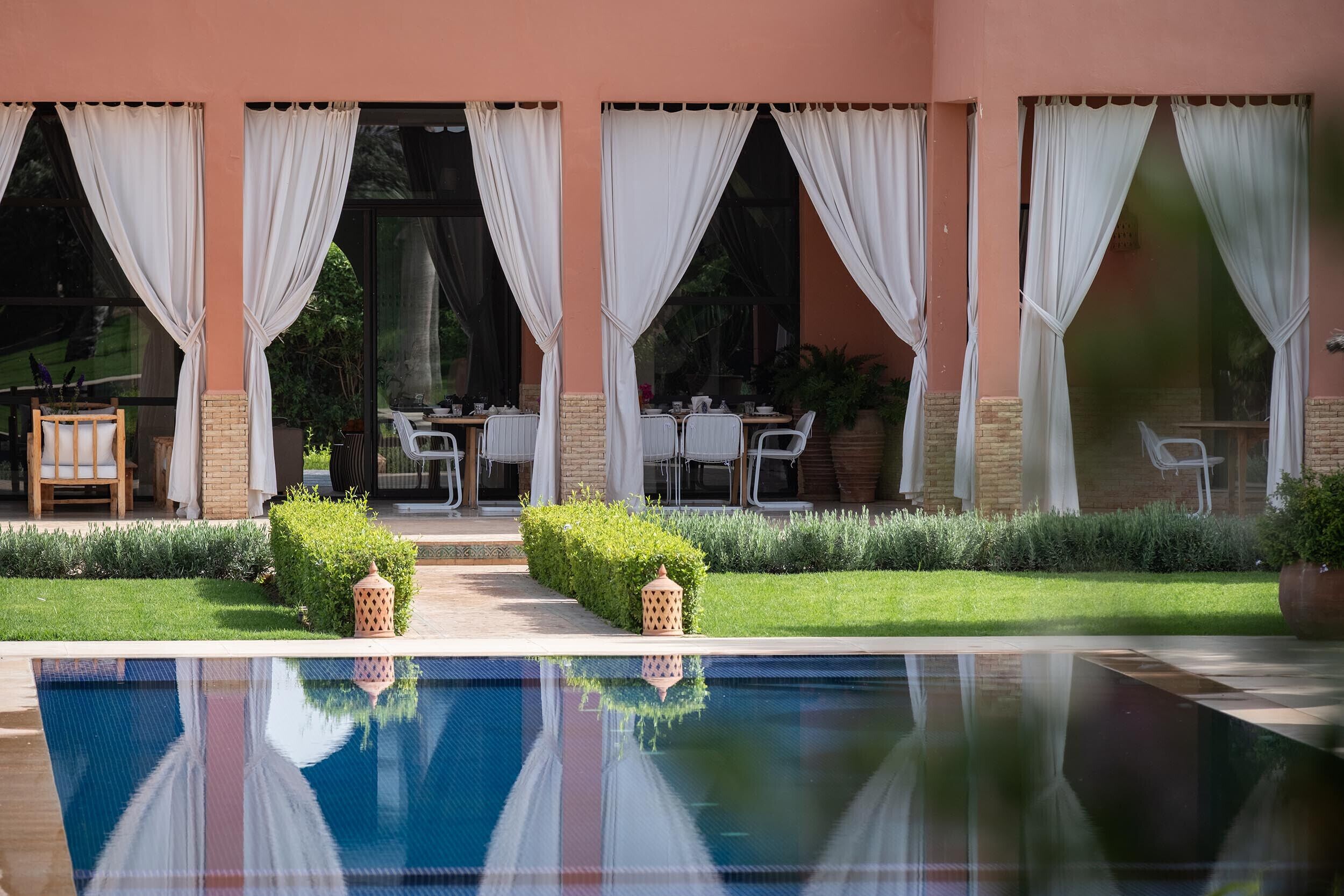 A poolside area with a clear view of the pool, a table with chairs, and a covered seating area with curtains.