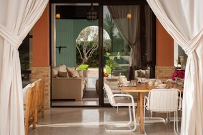 Une pièce moderne comprenant un canapé, une table à manger, des chaises et une porte-fenêtre coulissante donnant sur un espace extérieur agrémenté de plantes.