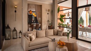 A modern living room with a beige sofa, a round coffee table with striped cushions, and a large window with curtains. - Villa Chocolat - Private pool - Perfect for relaxed  - (7 rms/14 Gst) (Marrakech)