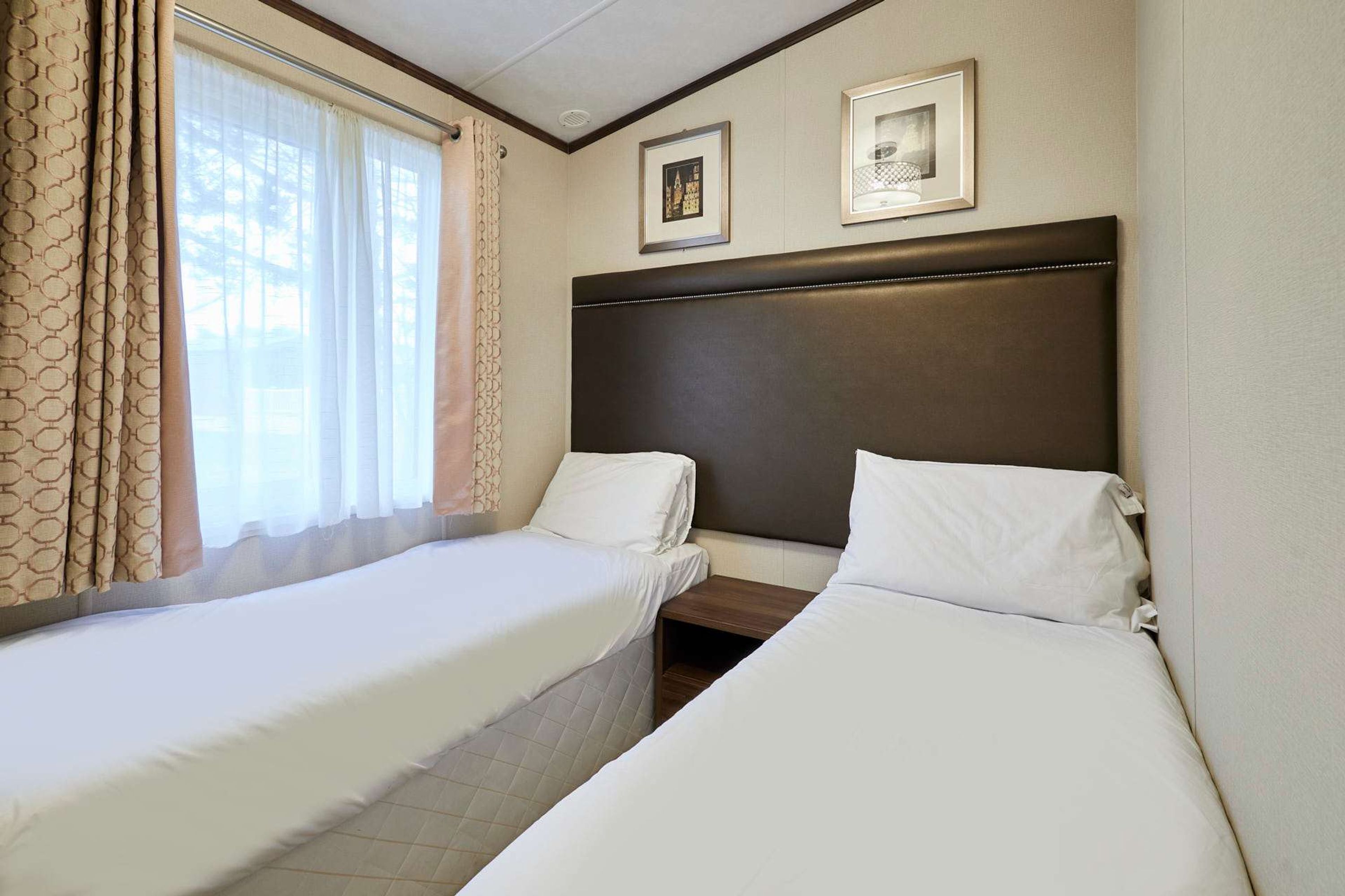Ett hotellrum med två separata sängar, ett fönster med gardiner och inramade tavlor på väggen.