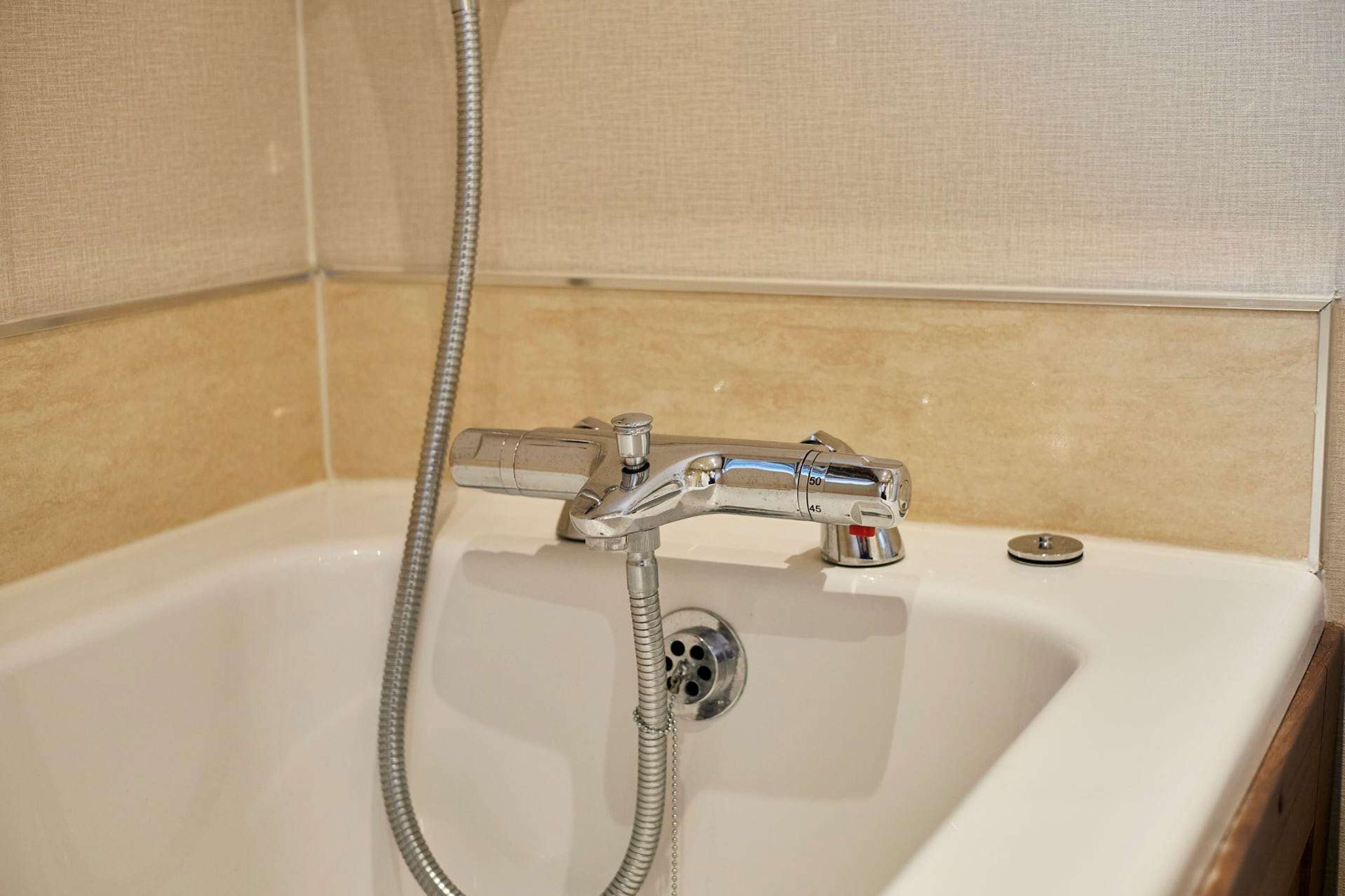 Un baño con lavamanos blanco, grifo cromado y ducha de mano.