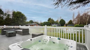 A hot tub on a wooden deck with outdoor furniture, surrounded by a white fence and trees. - Host Stay Sutton Lodge (York)