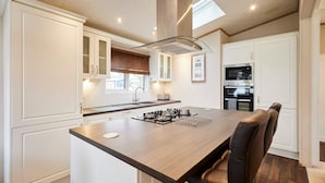 A modern kitchen with white cabinetry, a central island with a gas stove, and a dining area with a brown leather chair. - Host Stay Sutton Lodge (York)