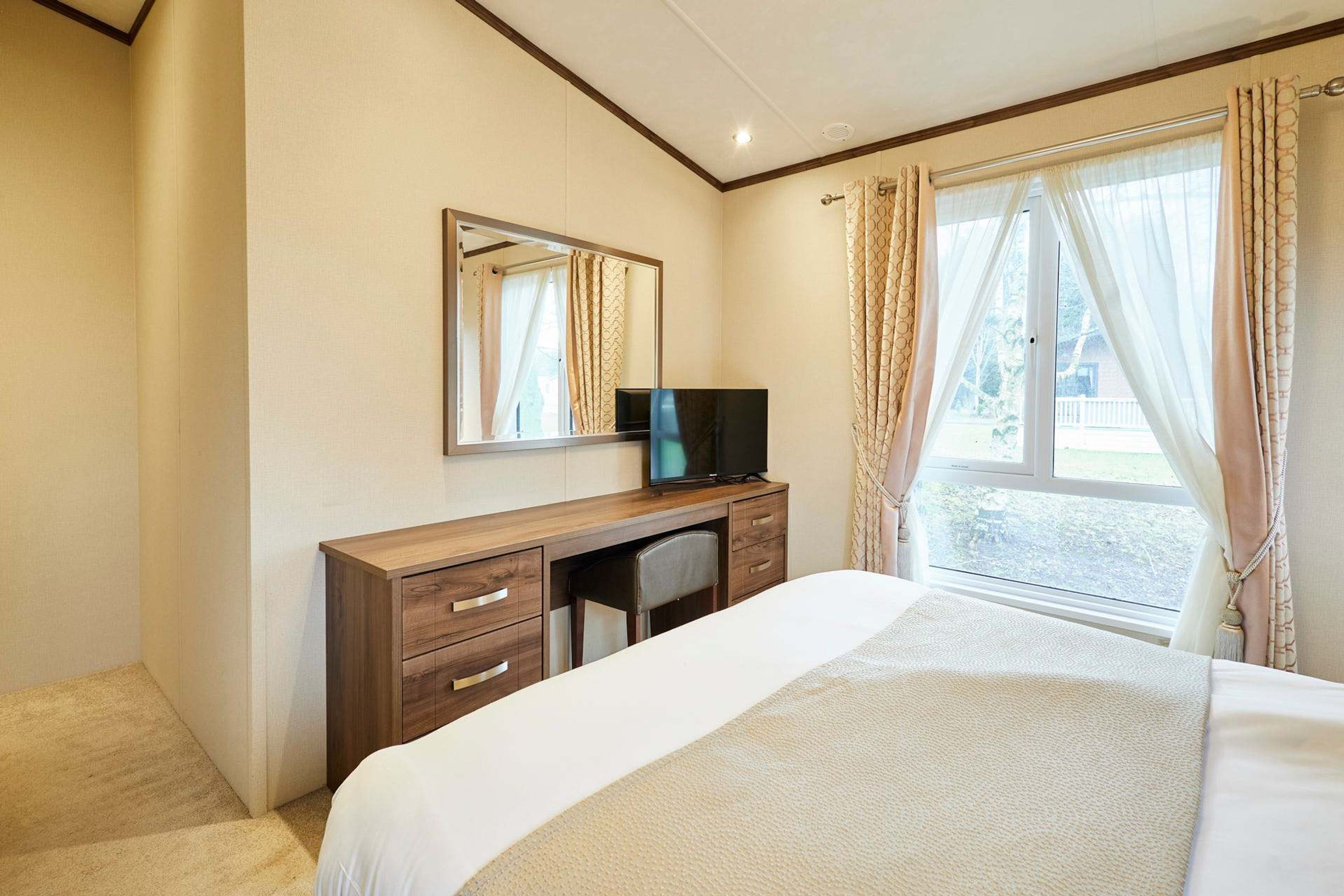 Una habitació d'hotel amb un llit, un escriptori de fusta amb televisió, un mirall i una finestra amb cortines.