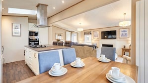 A modern kitchen with a central island, dining area with a wooden table set for four, and a cozy living space with a fireplace. - Host Stay Sutton Lodge (York)