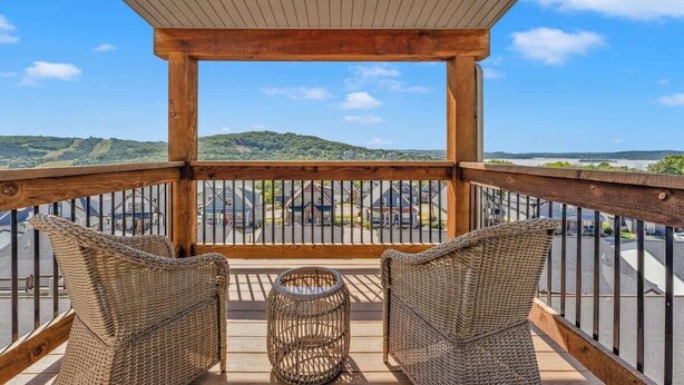 A wooden deck with wicker furniture and a wicker table, overlooking a parking area and distant hills. - Hooked on Branson Cove - Pool Hot Tub Fireplace (Hollister)