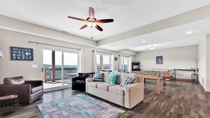A spacious living room with a foosball table, a ceiling fan, and a large window offering a view of the outdoors. - Hooked on Branson Cove - Pool Hot Tub Fireplace (Hollister)